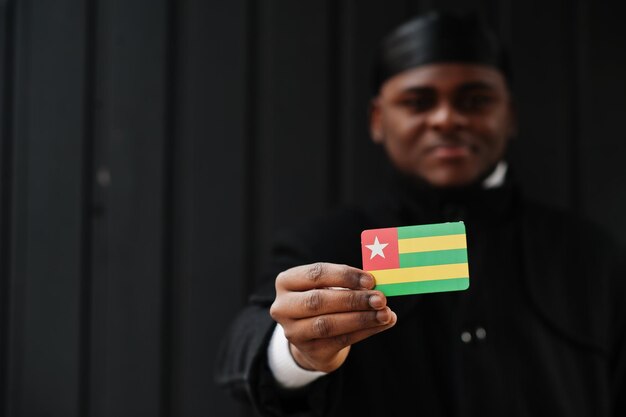 L'uomo africano indossa il durag nero tiene la bandiera del Togo a portata di mano isolata su sfondo scuro