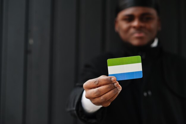 L'uomo africano indossa il durag nero tiene la bandiera della Sierra Leone a portata di mano isolata su sfondo scuro