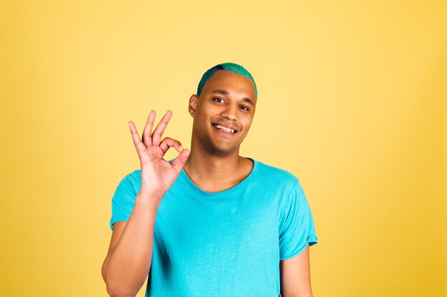 L'uomo africano nero in casual sullo sguardo felice della parete gialla alla macchina fotografica con il gesto giusto di manifestazione di sorriso