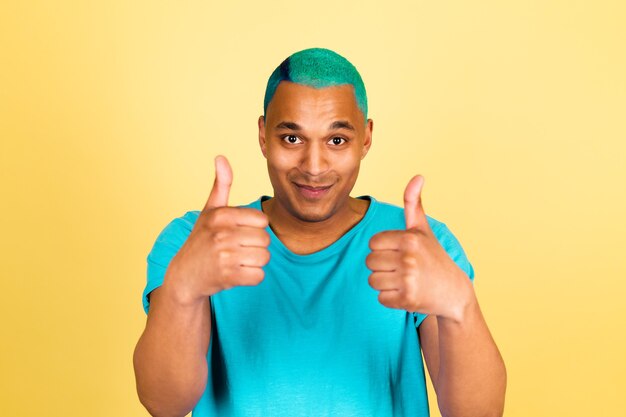 L'uomo africano nero in casual sullo sguardo positivo felice della parete gialla alla macchina fotografica mostra i pollici in su è d'accordo