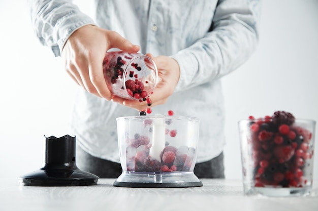 L'uomo aggiunge bacche congelate alla pentola del frullatore concentrato prima di preparare un gustoso frullato da bere per rinfrescarsi nel periodo estivo. Vetro sfocato con bacche congelate davanti vicino