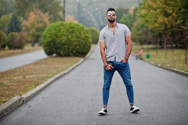 L'uomo alla moda con barba araba alta indossa su camicia jeans e occhiali da sole in posa sul parco e tieni il portafoglio a portata di mano