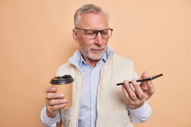 L'uomo anziano barbuto dai capelli grigi guarda attentamente i nuovi smartphone esamina i nuovi gadget
