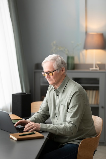 L'uomo anziano sta usando il computer portatile seduto alla scrivania in soggiorno