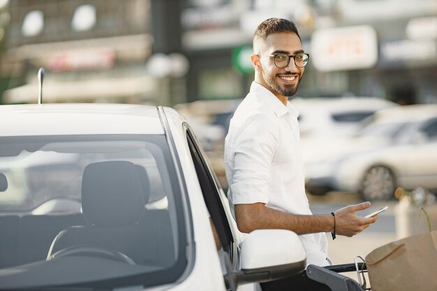 L'uomo arabo usa lo smartphone mentre aspetta di caricare la batteria in macchina. Consapevolezza ecologica.