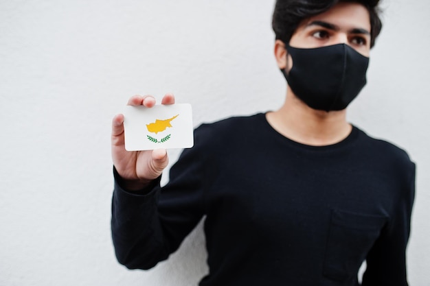 L'uomo asiatico indossa tutto nero con maschera facciale tiene in mano la bandiera di Cipro isolata su sfondo bianco Concetto di paese di coronavirus