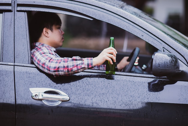 l'uomo asiatico tiene una bottiglia di birra mentre sta guidando una macchina
