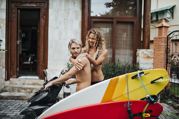 L'uomo aspetta che la sua ragazza si sieda sulla moto con le tavole da surf allegate