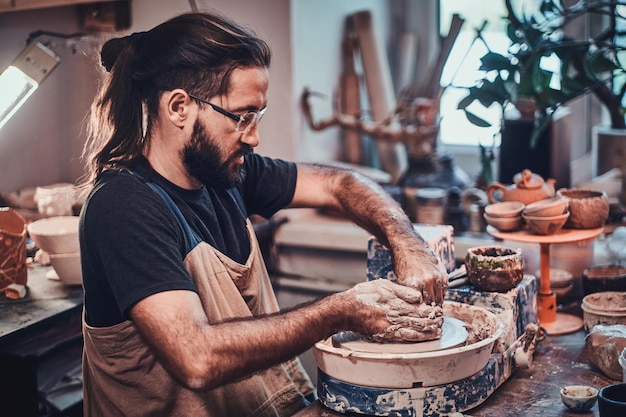 L'uomo attraente con gli occhiali sta lavorando al suo progetto di argilla.