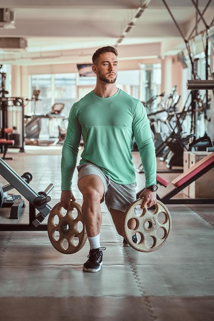 L'uomo attraente e sportivo in camicia da allenamento verde sta facendo i suoi esercizi in palestra con i pesi.