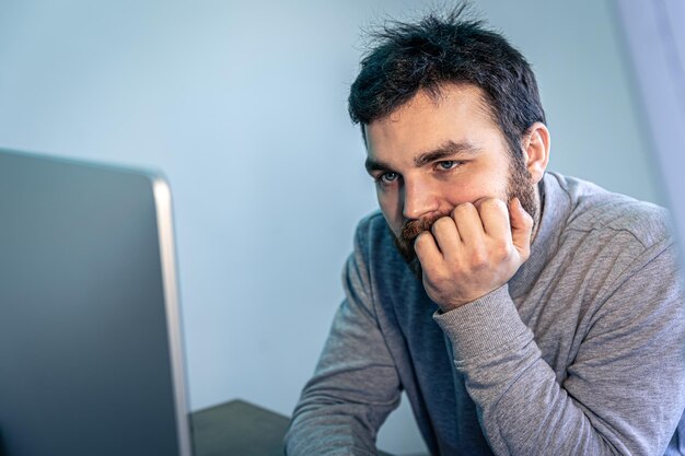 L'uomo barbuto stanco guarda lo schermo del computer