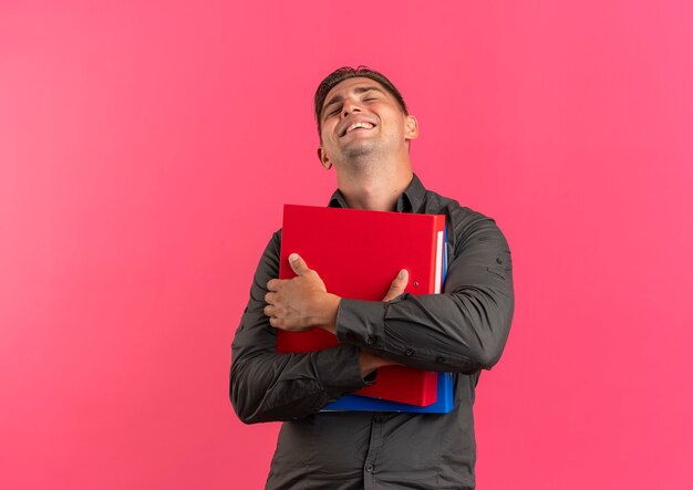 L'uomo bello biondo felice giovane tiene le cartelle di file isolate su fondo rosa con lo spazio della copia