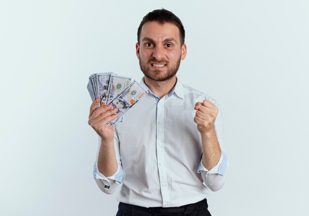 L'uomo bello furioso tiene i soldi e tiene il pugno isolato sul muro bianco