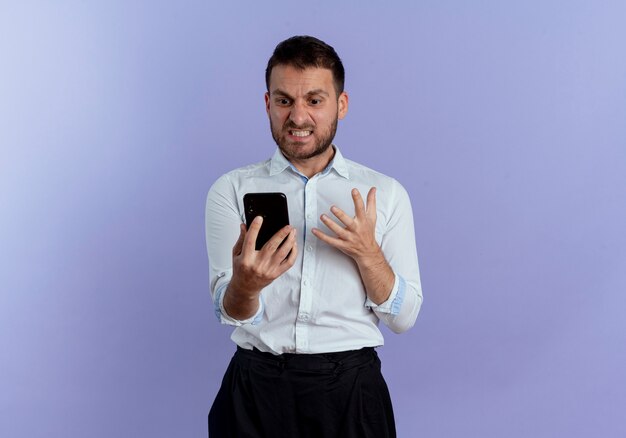 L'uomo bello infastidito tiene e guarda il telefono isolato sulla parete viola