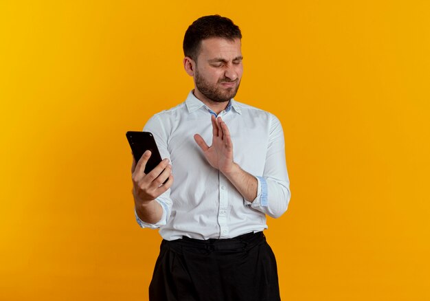 L'uomo bello infastidito tiene il telefono isolato sulla parete arancione