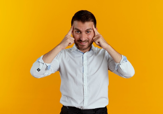 L'uomo bello sorridente mette le dita sulle tempie isolate sulla parete arancione