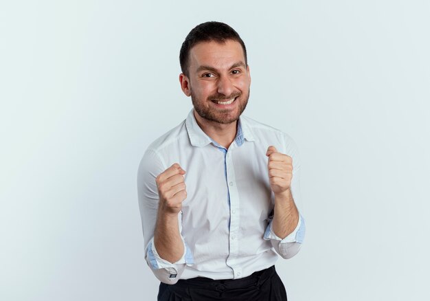 L'uomo bello sorridente tiene i pugni isolati sulla parete bianca