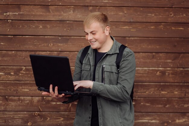 L'uomo bello sta usando un computer portatile e un telefono all'aperto sulla parete di legno