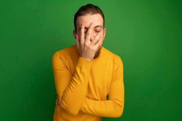 L'uomo biondo bello deluso mette la mano sulla faccia sul verde