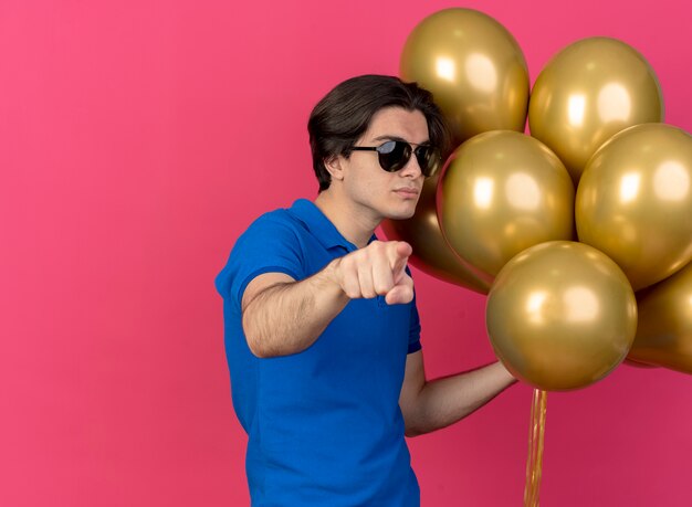 L'uomo caucasico bello sicuro in occhiali da sole tiene palloncini di elio che puntano alla telecamera