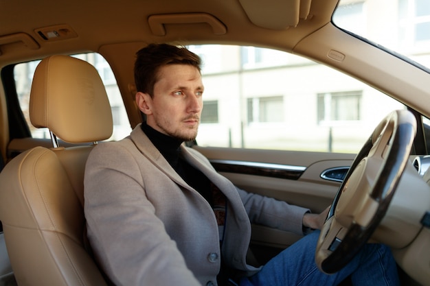 L'uomo caucasico bello sta guardando attraverso il parabrezza nel nuovo salone beige dell'automobile