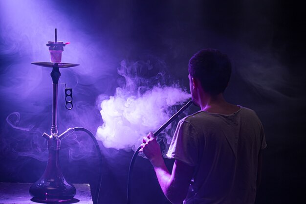 L'uomo che fuma il classico Shisha. Bellissimi raggi colorati di luce e fumo. Il concetto di fumo di narghilè.