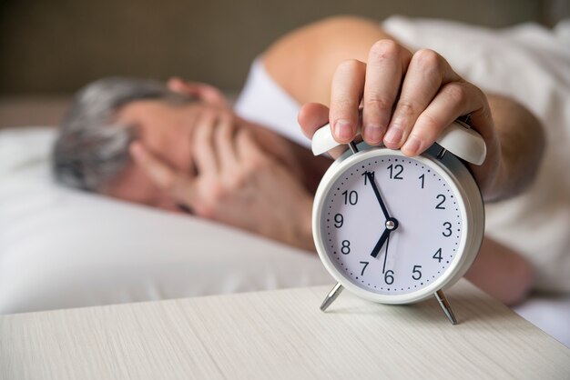 L&#39;uomo che giaceva a letto spegne una sveglia la mattina alle 7 del mattino. Uomo attraente che dorme nella sua camera da letto. Un uomo malignato risvegliato da una sveglia nella sua camera da letto