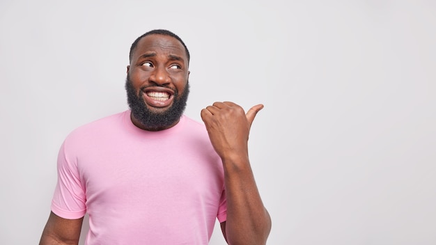 l'uomo con i denti bianchi punta il pollice sullo spazio vuoto mostra il posto per il logo o il posizionamento del prodotto vestito con una maglietta rosa casual casual