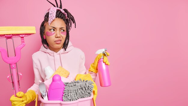 l'uomo con i dreadlocks tiene il detersivo spray e il mop sorride con il viso isolato sul rosa