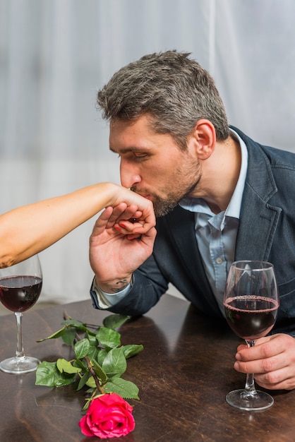 L&#39;uomo con il bicchiere di vino che bacia la mano della donna alla tavola con è aumentato