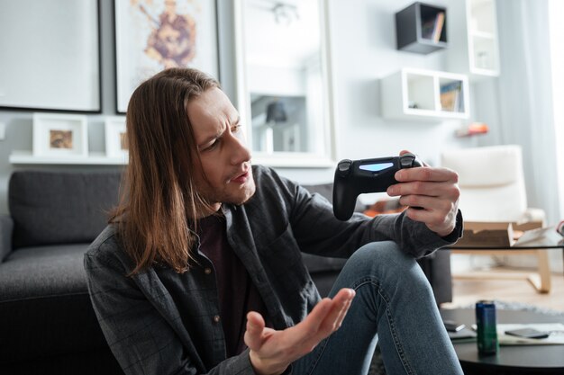 L'uomo confuso che si siede a casa all'interno gioca con il joystick.