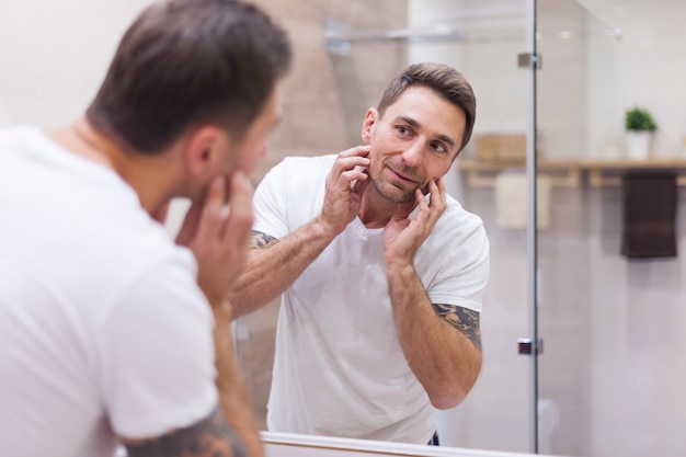 L'uomo controlla le condizioni della sua pelle nel riflesso dello specchio