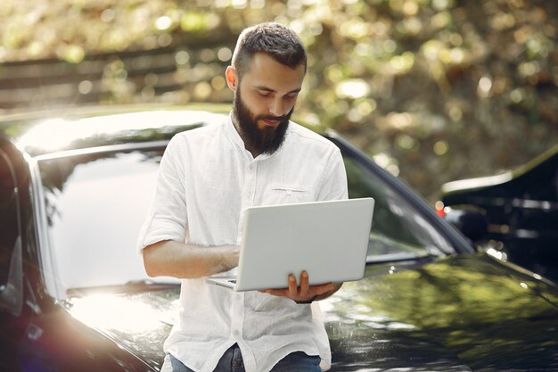 L'uomo d'affari alla moda che sta vicino all'automobile e usa il computer portatile