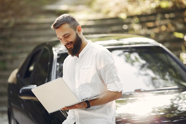 L'uomo d'affari alla moda che sta vicino all'automobile e usa il computer portatile