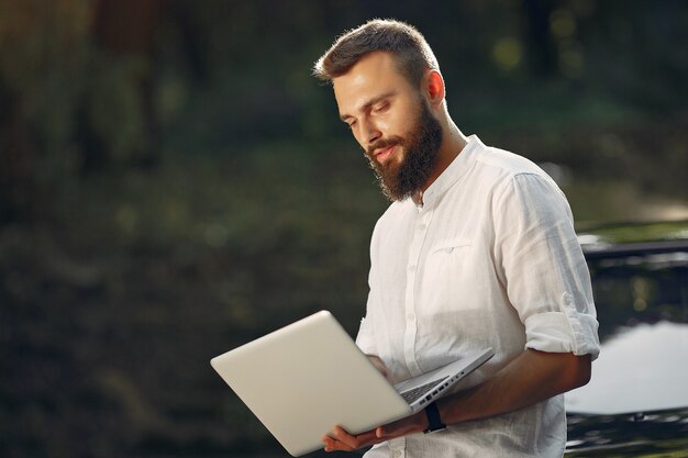 L'uomo d'affari alla moda che sta vicino all'automobile e usa il computer portatile