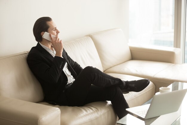 L&#39;uomo d&#39;affari comunica sul telefono mentre si siede sullo strato.