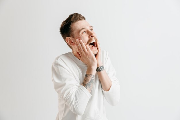 L'uomo d'affari felice in piedi e sorridente contro il muro grigio.