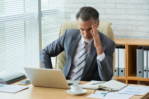 L'uomo d'affari si è concentrato sui dati del computer che toccano la sua testa nell'emicrania