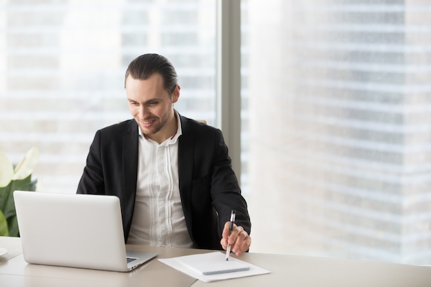 L&#39;uomo d&#39;affari sorridente felice in ufficio che esamina il computer portatile sreen.