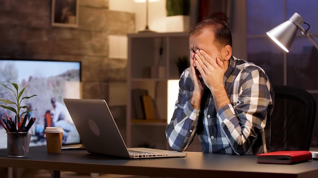 L'uomo d'affari stanco sbadiglia e si stropiccia gli occhi in ufficio a casa durante le ore notturne. Uomo d'affari oberato di lavoro.