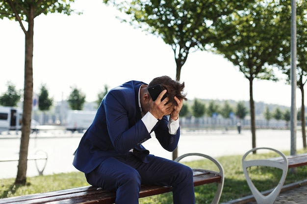 L&#39;uomo d&#39;affari triste si siede sulla banca fuori della strada