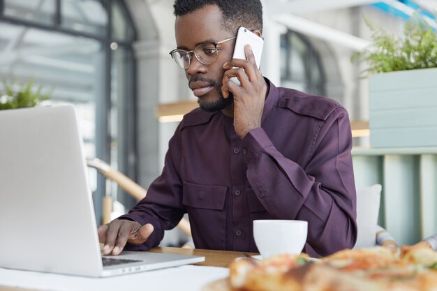 L'uomo dalla pelle scura concentrato in abbigliamento formale guarda con sicurezza nel computer portatile, ha un'espressione seria