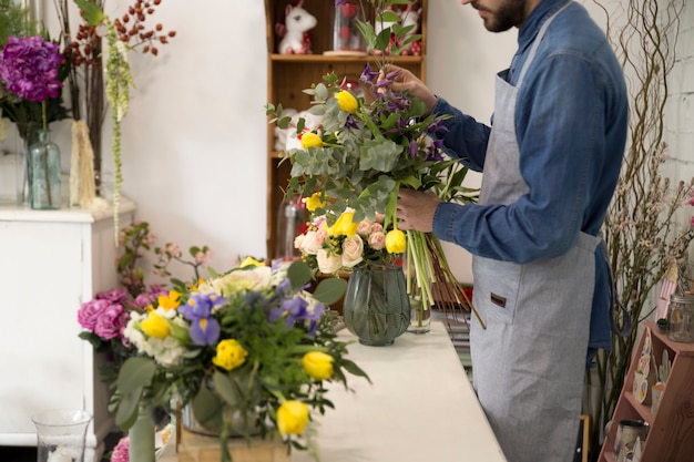 L&#39;uomo del fiorista in grembiule fa un mazzo nel negozio di fiori per un regalo festivo per un matrimonio o un anniversario