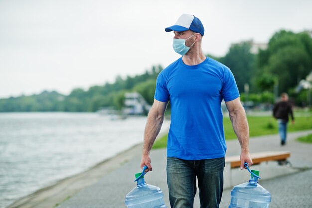L'uomo dell'acqua di consegna indossa una maschera medica protettiva per il viso durante la pandemia di coronavirus