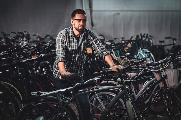 L'uomo diligente e laborioso in camicia a scacchi sta lavorando con le biciclette in un magazzino affollato.