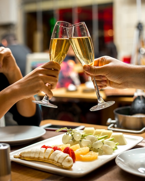 L'uomo e la donna bevono champagne con la banana del piatto di frutta con le fragole e l'uva