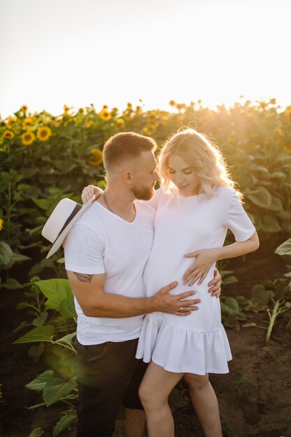 L'uomo e la donna incinta si abbracciano tenero in piedi nel campo con alti girasoli intorno a loro