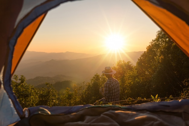 L&#39;uomo felice con la tazza di caffè della tenuta resta vicino alla tenda intorno alle montagne