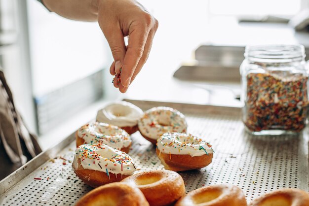 L'uomo fornaio spruzza ciambelle con dolci colorati