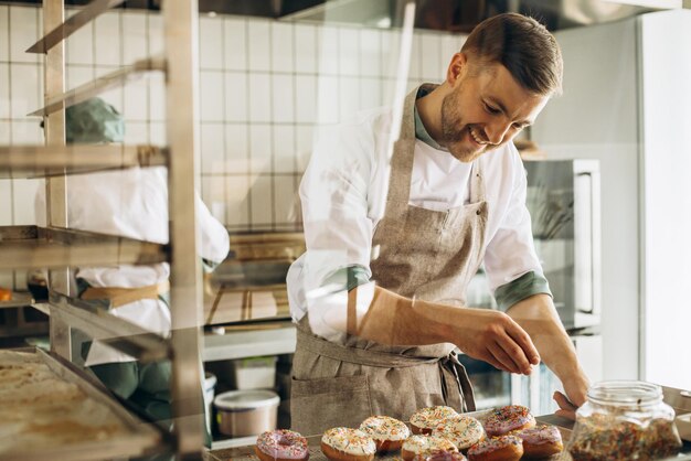 L'uomo fornaio spruzza ciambelle con dolci colorati